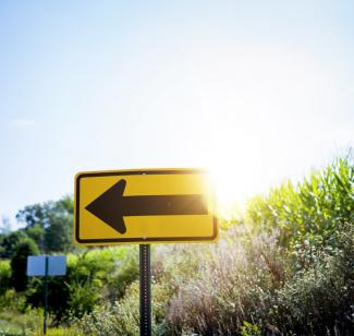 Gelbes Schild, im Hintergrund grüne Pflanzen und die niedrig stehende Sonne