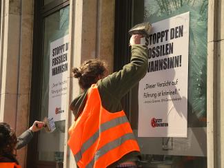 Mensch plakatiert Fenster mit "Stoppt den fossilen Wahnsinn"