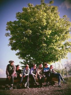 Menschen sitzen auf einer Bank vor einem Baum.